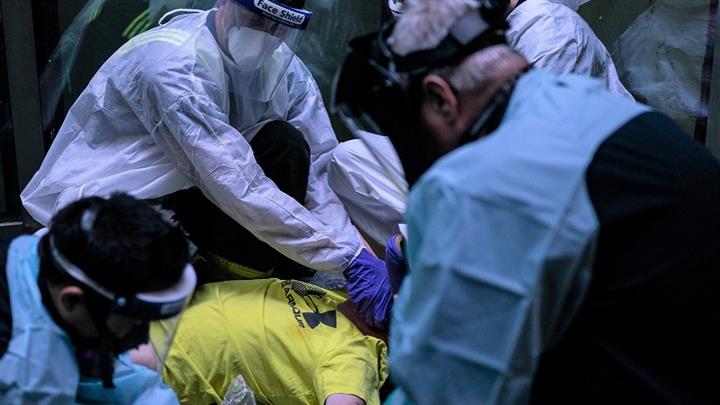 Paramedics in personal protective equipment assisting a patient on the ground