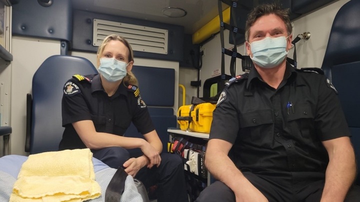 Two smiling paramedics sitting in an ambulance wearing masks