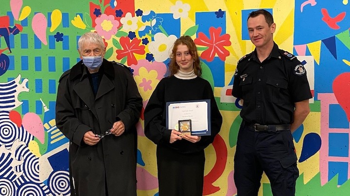 Madison receives an award for doing CPR, standing beside the man she saved and a responding paramedic