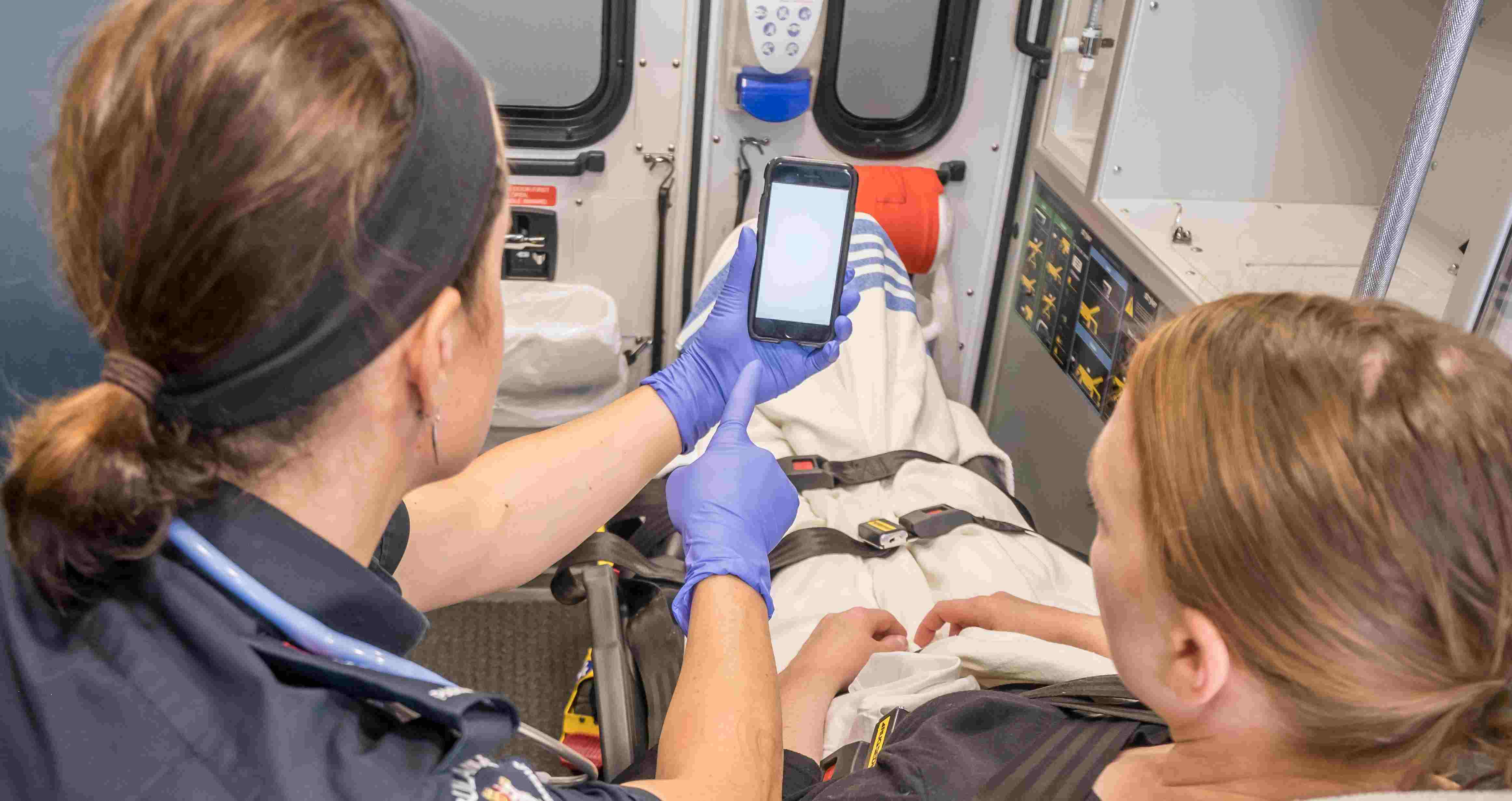 Stock photo of paramedic navigating their phone next to a patient