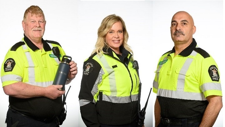 Three paramedics wearing summer uniforms in navy and bright yellow with high-visibility strips